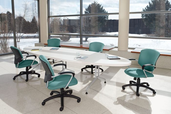 Studio photograph of five Supra rolling chairs placed at a long oval conference table. Tall and wide paned windows show a snowy area of trees.