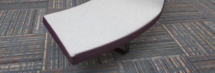 Studio shot of a curved bench, resting atop Relativity carpeting. Each square was given a quarter turn. The bench has been given a white cushion.