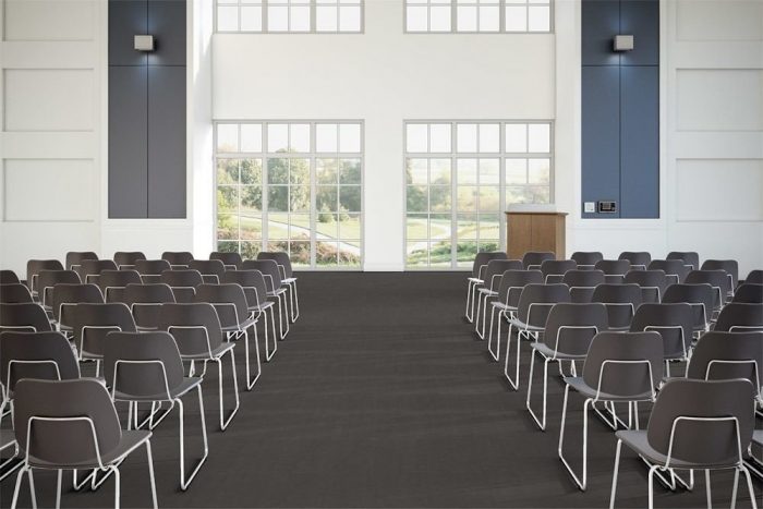 Flooring in a large lecture hall, using Transit's Gate color choice. A center aisle divides rows of medium backed metal framed chairs. Two windows in front look out to a grassy field.