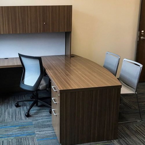 Run II mid-back chair behind a wood laminate L-shaped desk. There are two guest chairs placed in front of the desk, with the exit door off to the side.
