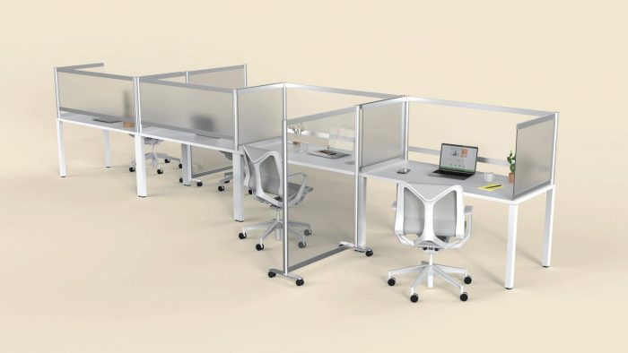 A long desk set for eight office workers. Desk Shields are placed at each seat, with an open laptop on one desk. Between the two nearest seats,a full length Split panel divides two workers.