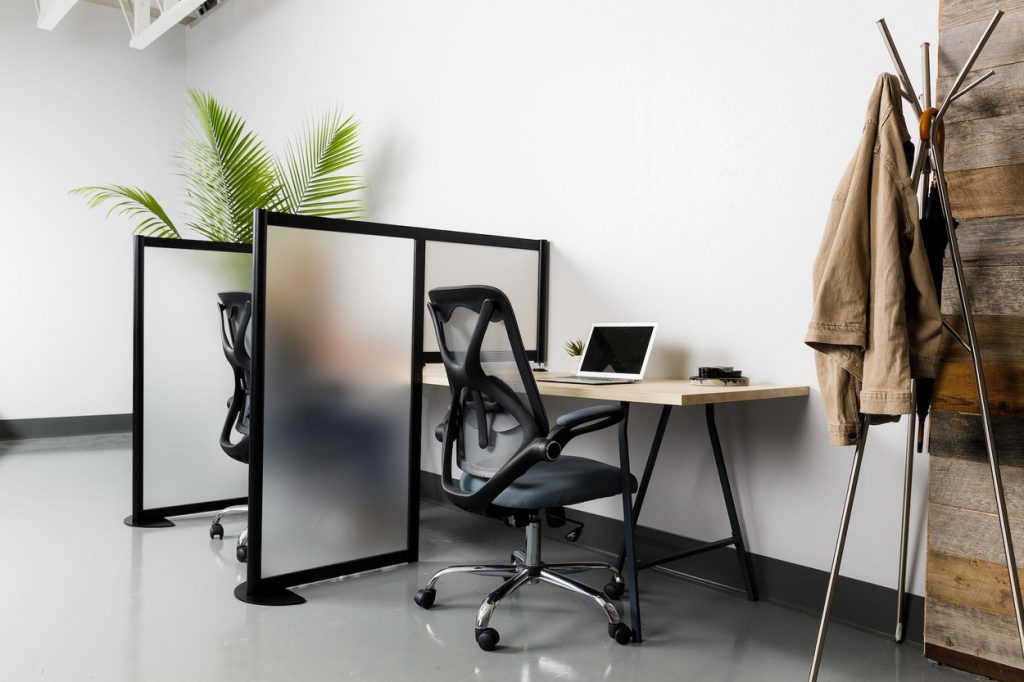 A medium desk set for two office workers. A Hitch partition separates each station. The work desk nearest to us has a tripod-style coat rack to its right.